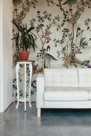 Sala de estar com sofá e suporte para planta brancos com painel chinoiserie ao fundo